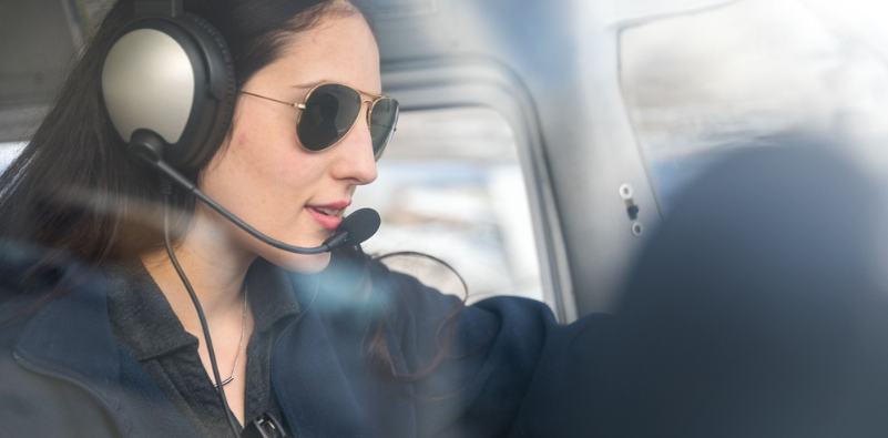 A female pilot in the cockpit of a plane wearing a pair of aviator sunglasses.