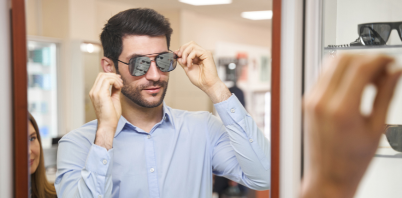A man looking at himself in a mirror while trying on sunglasses at the opticians